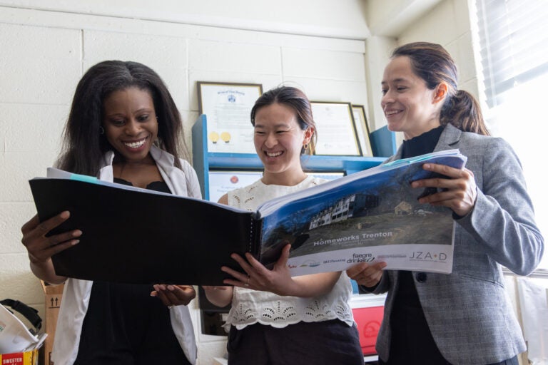 a HomeWorks Trenton dorm mom and two executives look at a book showing the future home of the organization