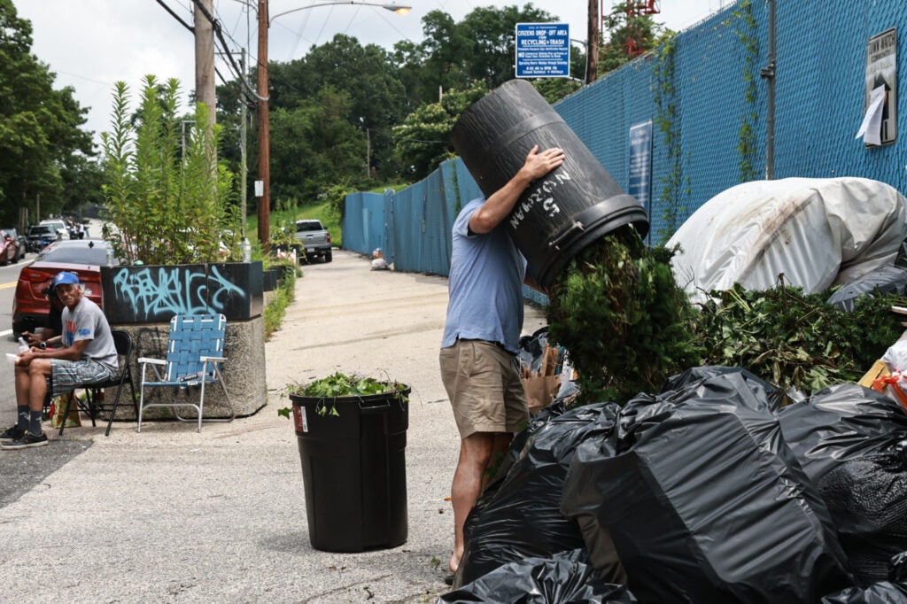 a person dumps yard trash onto bags of trash while a sanitation worker looks on at the Northwest Sanitation Convenience Center