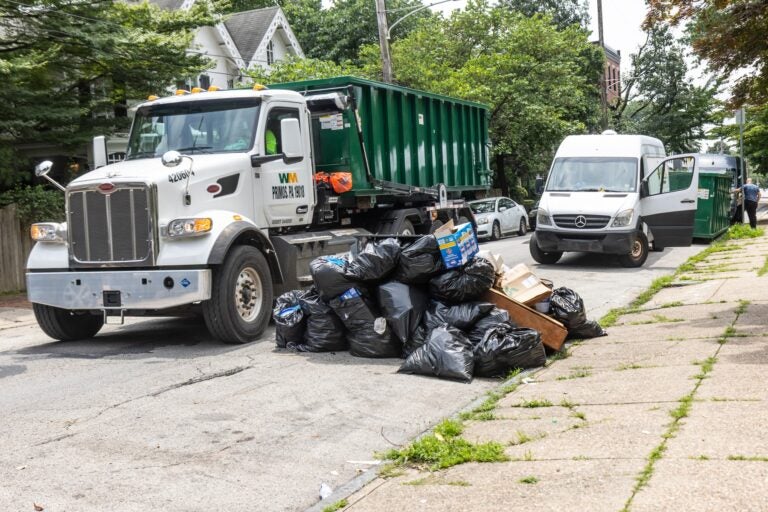 A dumpster is dropped off next to a pile of trash bags on Queen Lane