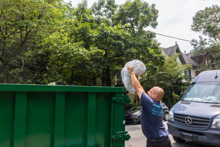 Ray Maldonado throws trash into a temporary dumpster on Queen Lane