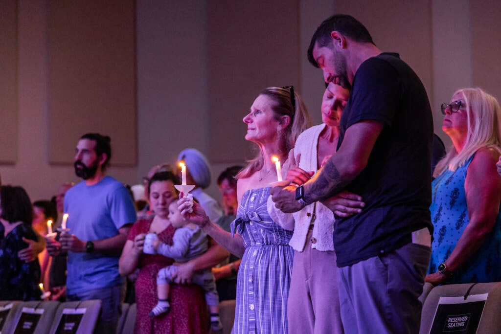 A person leans her head on the person next to her. Other people hold candles at a vigil.