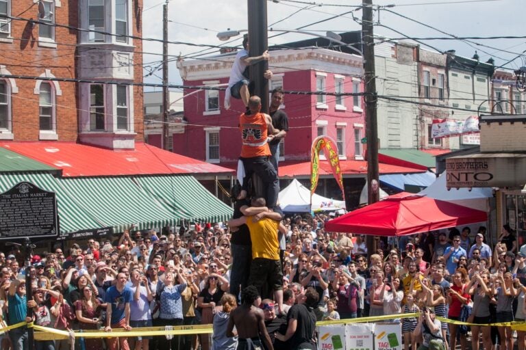 Many onlookers watch people climbing a greased pole