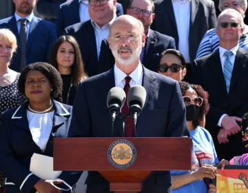 Gov. Tom Wolf speaks from a podium with people behind him