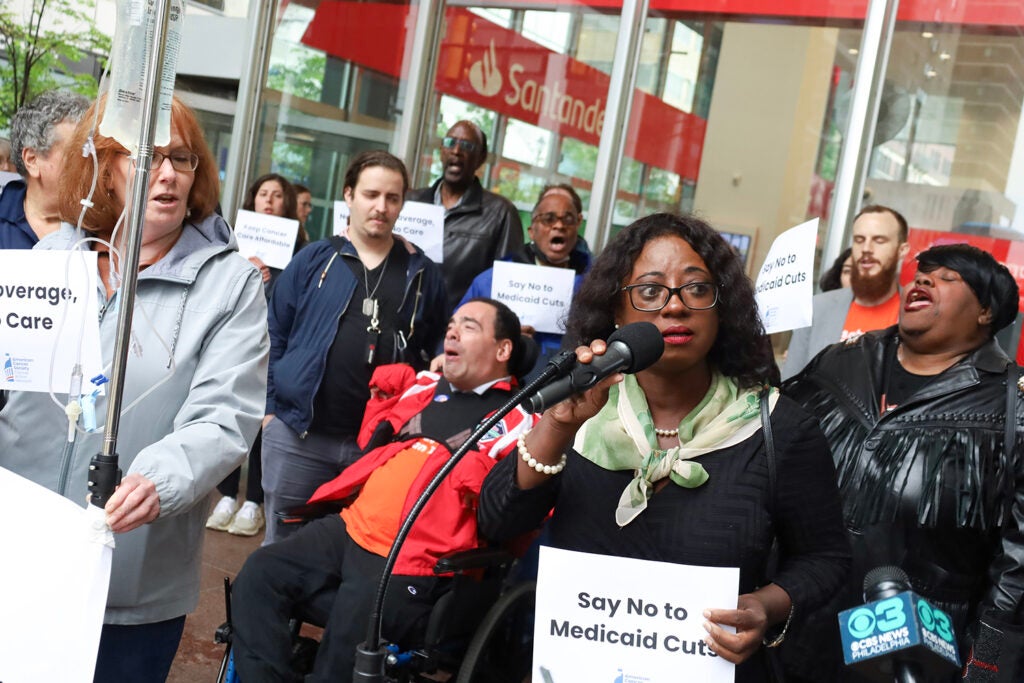 A woman speaks into a microphone at a rally against Medicaid cuts in Philadelphia
