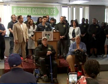 A number of union workers who work for Philadelphia stand behind a podium as they announce their vote to strike amid contract negotiations
