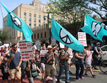 People march in Philadelphia holding signs and flags with the symbol for peace on them