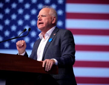 Minnesota Governor Tim Walz stands behind a podium with an American flag in the background