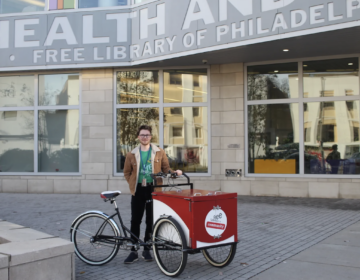 Tyler Gittelman poses for a picture with the Free Library's Book Bike outside the South Philly branch.